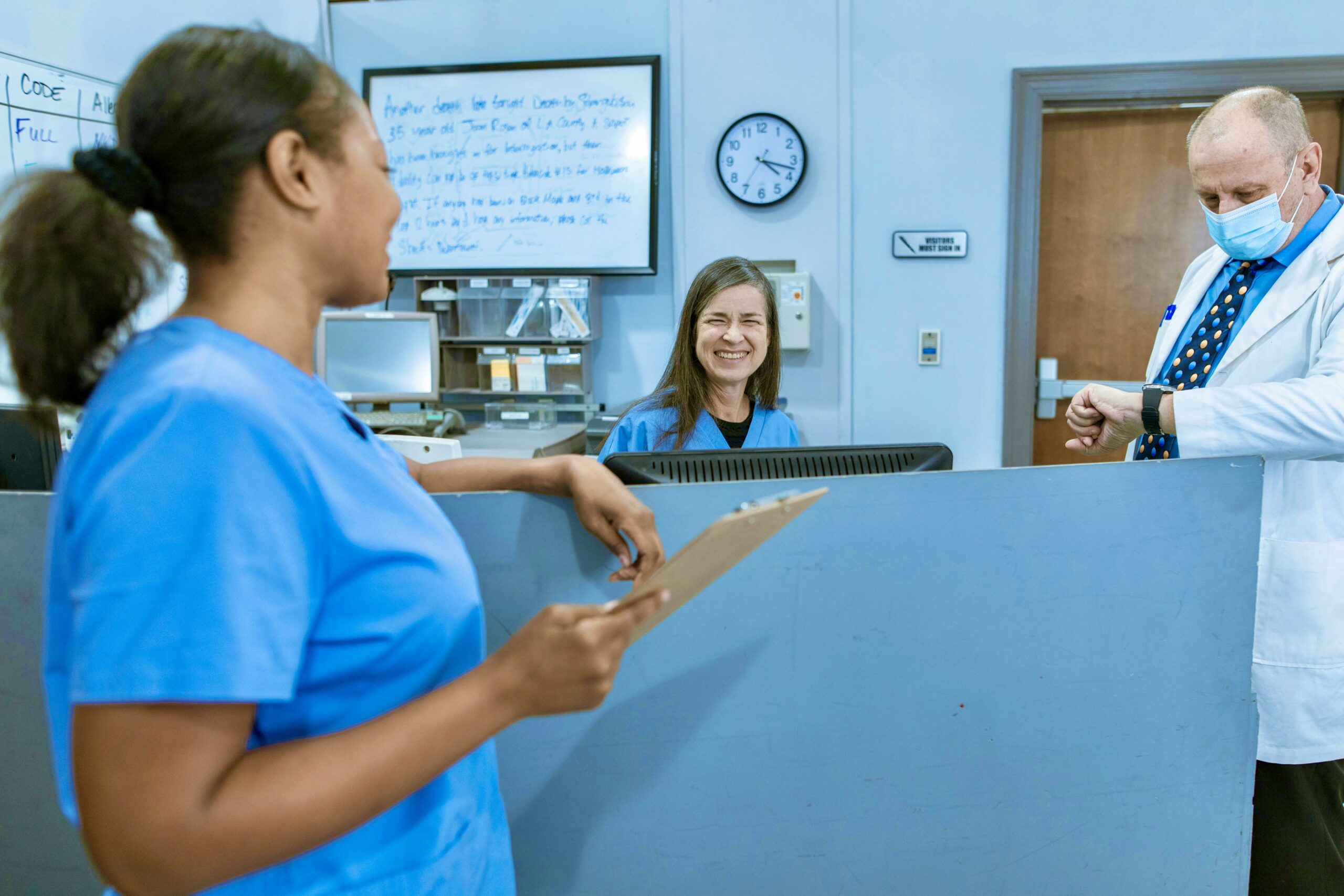 Image of two nurses and a doctor talking at the nurses station